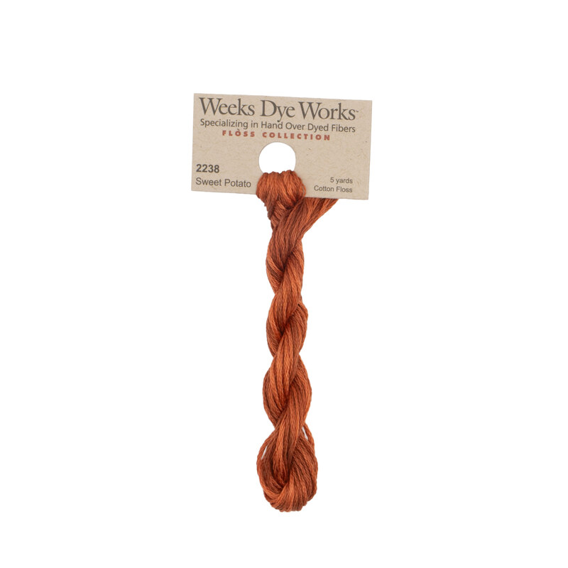 A skein of burnt sienna embroidery floss, twisted and bundled, with a tan label featuring the brand name and color information.