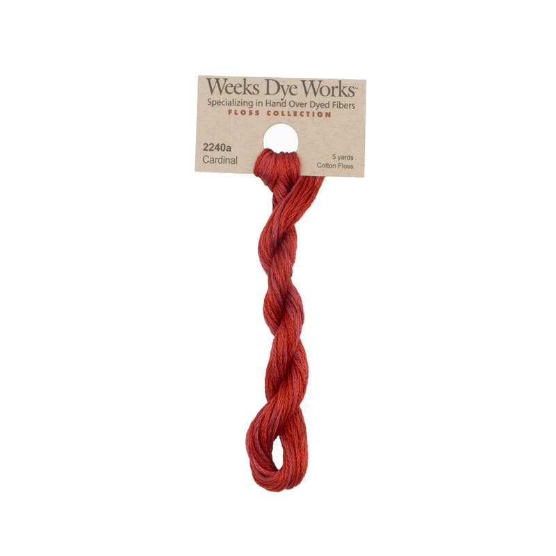 A skein of cranberry red embroidery floss, twisted and bundled, with a tan label featuring the brand name and color information.