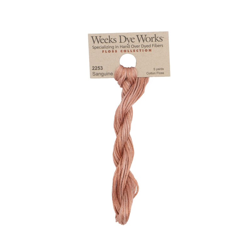 A skein of dark peach embroidery floss, twisted and bundled, with a tan label featuring the brand name and color information.