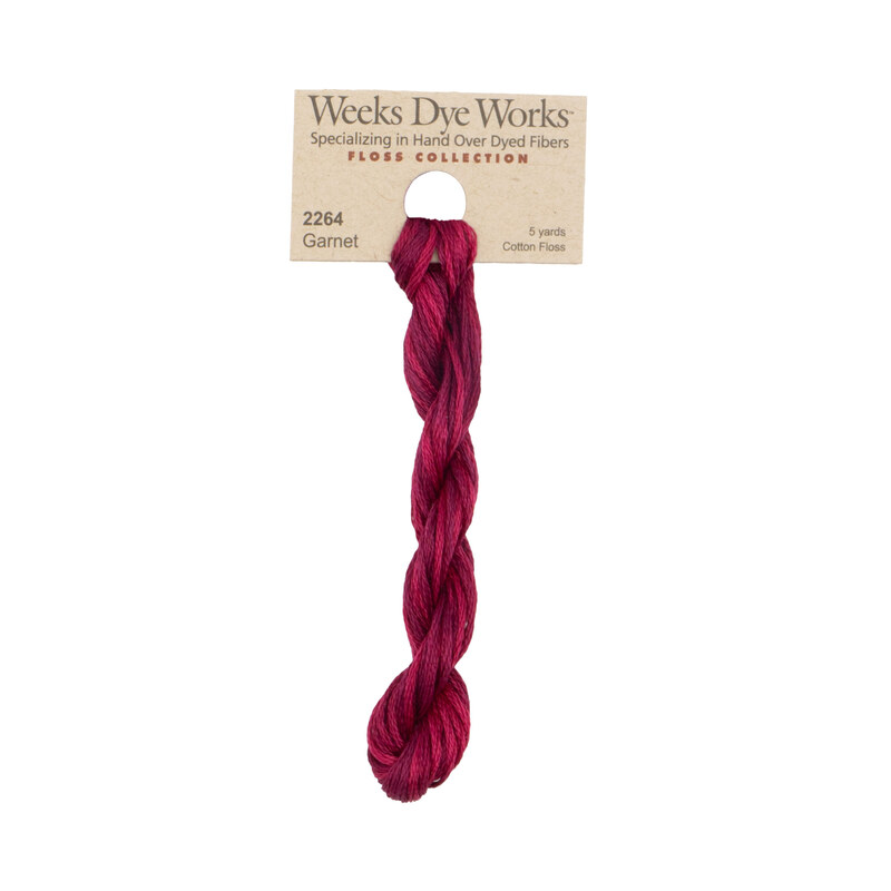 A skein of ruby red embroidery floss, twisted and bundled, with a tan label featuring the brand name and color information.?