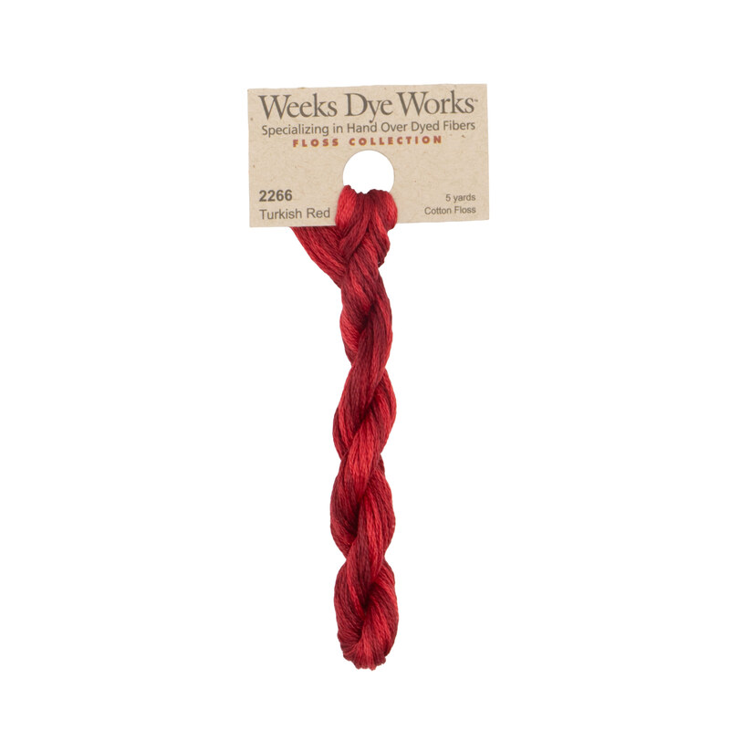 A skein of tonal crimson embroidery floss, twisted and bundled, with a tan label featuring the brand name and color information.?