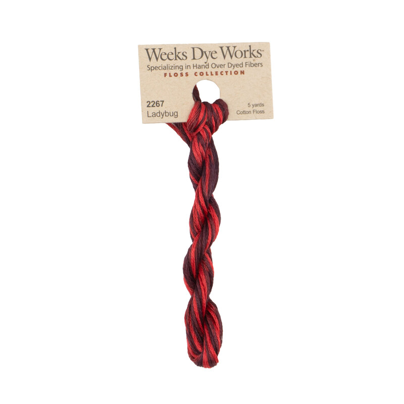 A skein of variegated black cherry and cranberry red embroidery floss, twisted and bundled, with a tan label featuring the brand name and color information.
