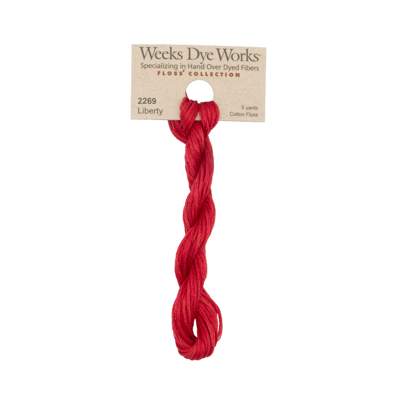 A skein of cherry red embroidery floss, twisted and bundled, with a tan label featuring the brand name and color information.