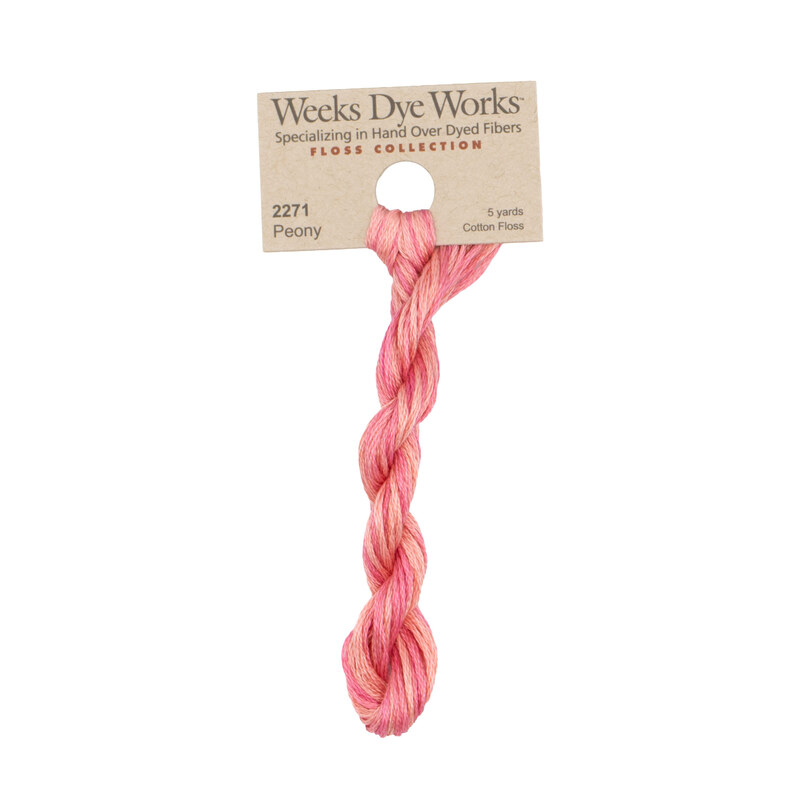 A skein of coral and bright pink embroidery floss, twisted and bundled, with a tan label featuring the brand name and color information.