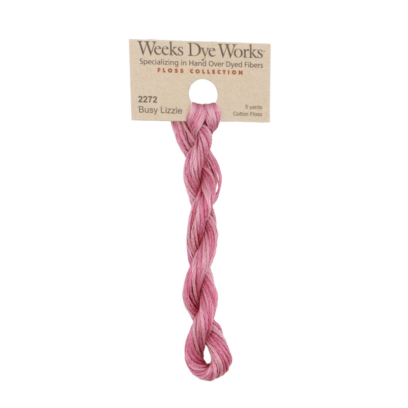 A skein of variegated light and dark pink embroidery floss, twisted and bundled, with a tan label featuring the brand name and color information.