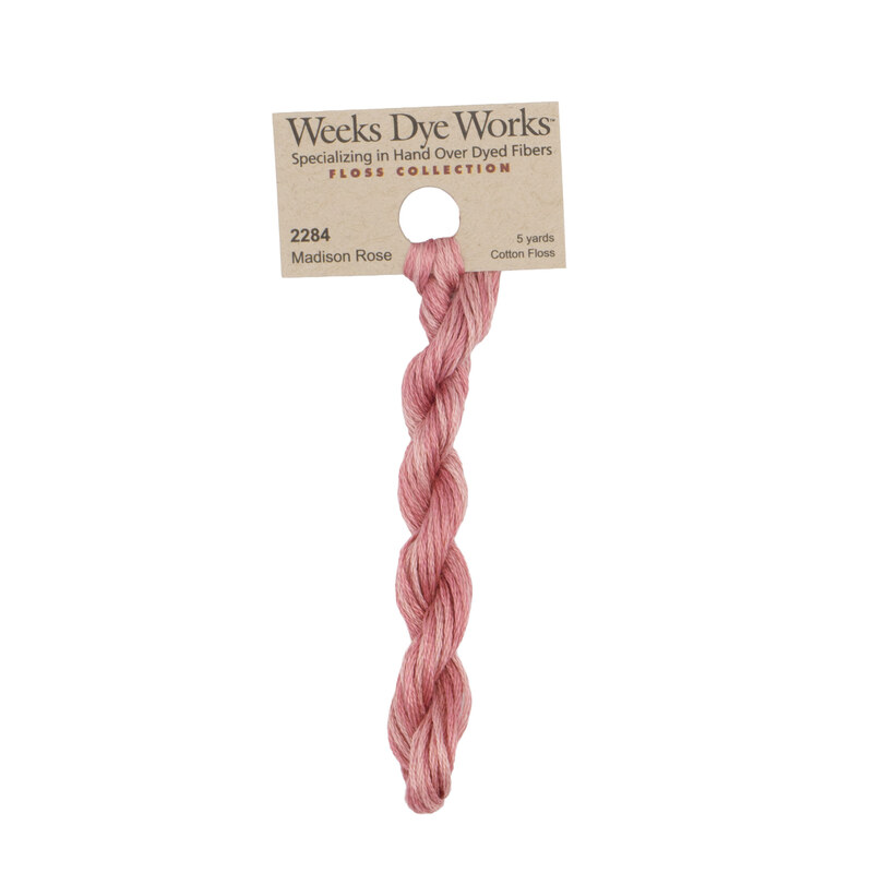 A skein of light rose embroidery floss, twisted and bundled, with a tan label featuring the brand name and color information.