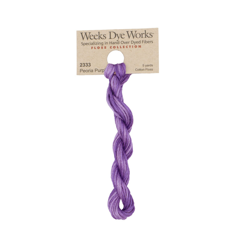 A skein of wisteria purple embroidery floss, twisted and bundled, with a tan label featuring the brand name and color information.