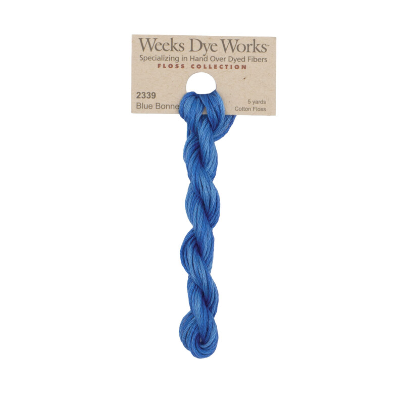A skein of cornflower blue embroidery floss, twisted and bundled, with a tan label featuring the brand name and color information.