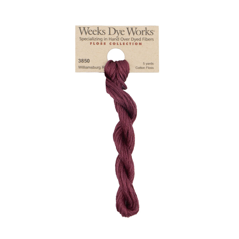 A skein of muted burgundy embroidery floss, twisted and bundled, with a tan label featuring the brand name and color information.