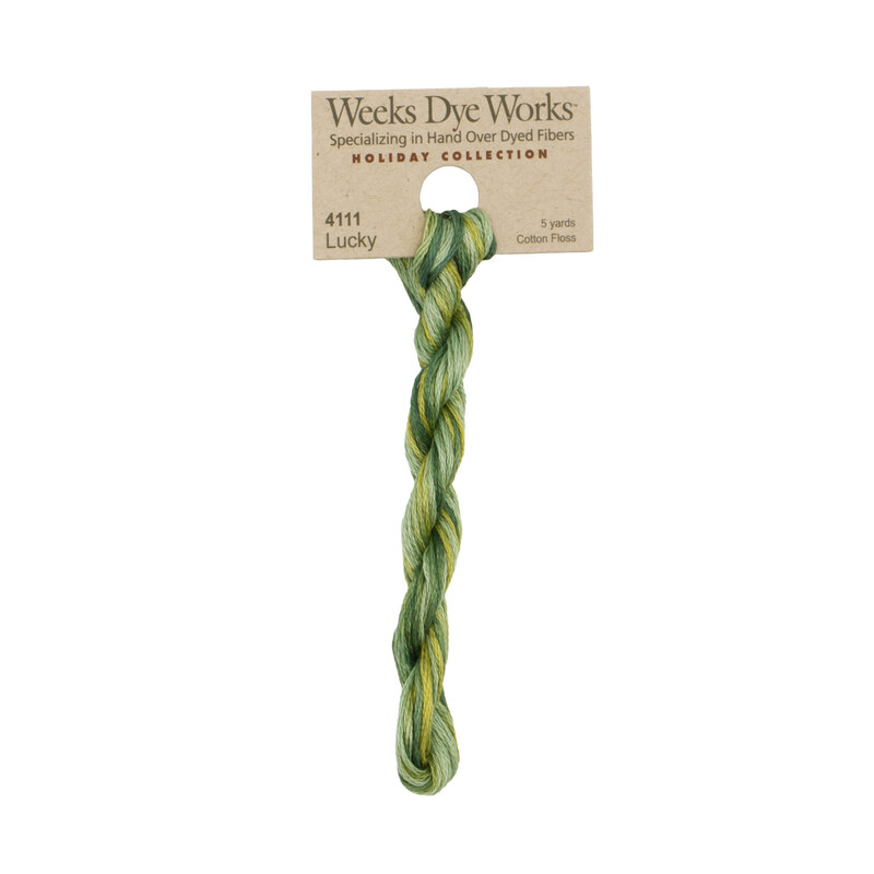 A skein of variegated green embroidery floss, twisted and bundled, with a tan label featuring the brand name and color information.