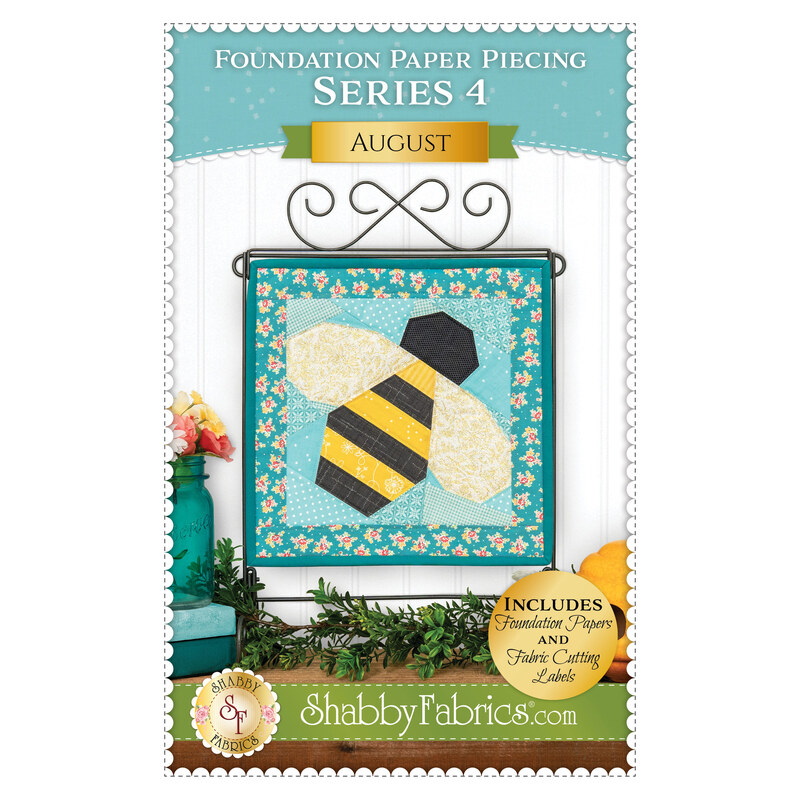 Front cover of the August pattern featuring the completed Foundation Paper Piecing Series 4 August project, a teal and yellow design of a bumblebee, displayed on a craft stand and staged with coordinating décor.