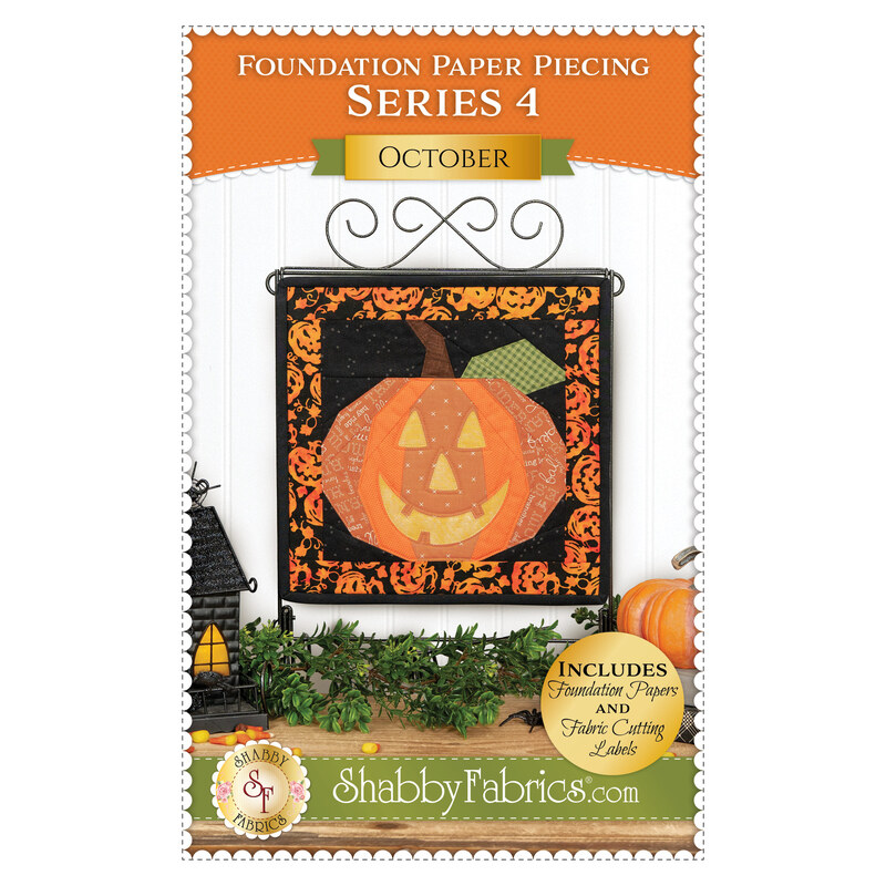 Front cover of the pattern showing the completed project colored in orange, black, yellow, and green fabrics, hung on a display hanger against a white paneled wall.