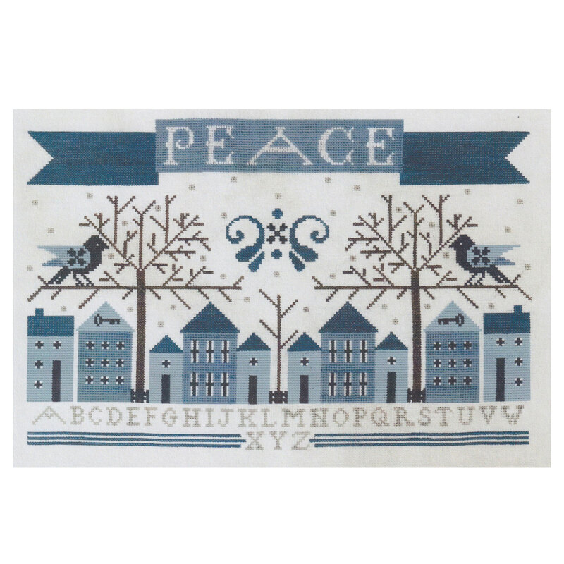 A stitched sampler featuring blue houses, snowflakes, and the word PEACE surrounded by alphabet letters.
