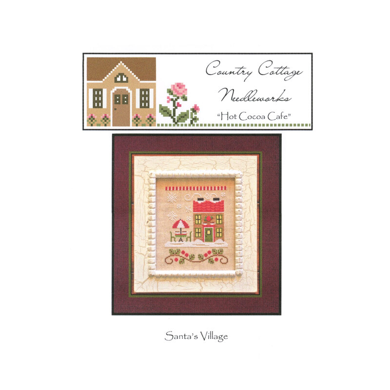 The front image of the "Hot Cocoa Cafe" cross stitch pattern featuring an umbrella covered table and a building with a snowy background.