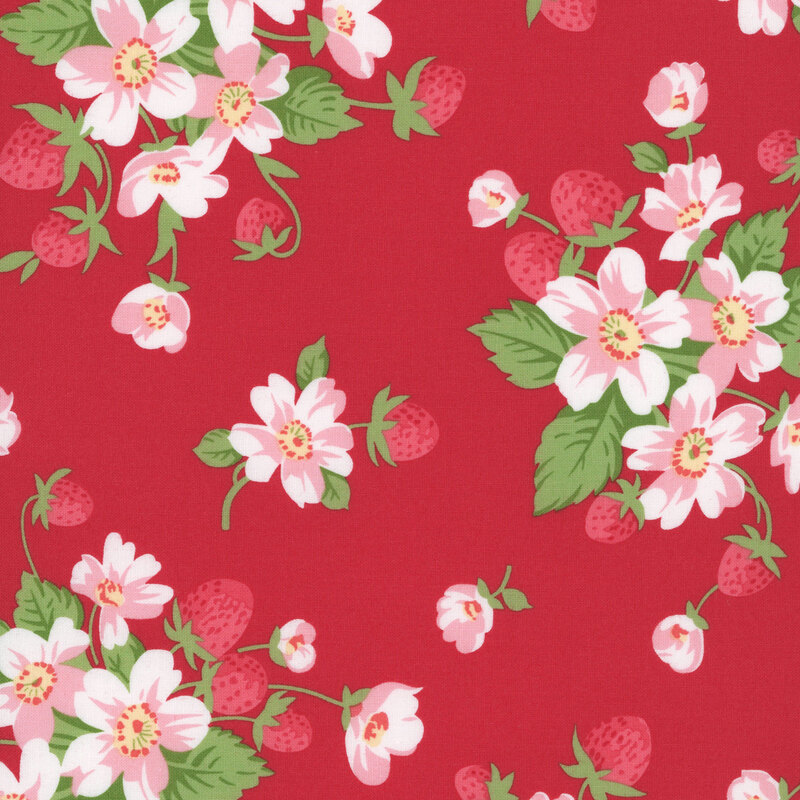 A red fabric with bunches of strawberry plants with pink flowers. 