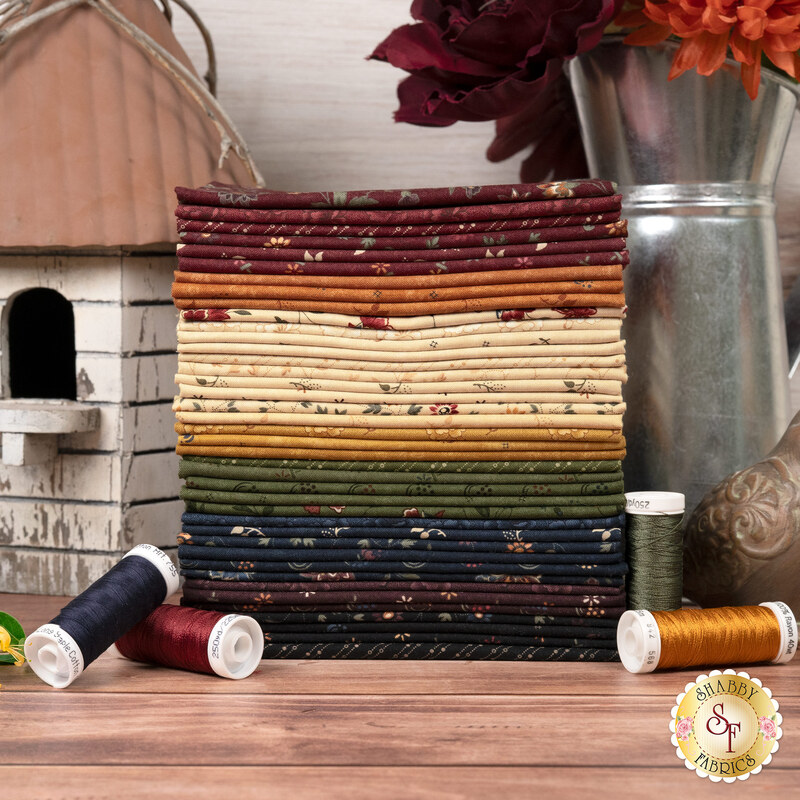 A stack of the fabrics included in the Honeysuckle Farm Fat Eighth Bundle, with flowers in a pitcher and a birdhouse and thread.