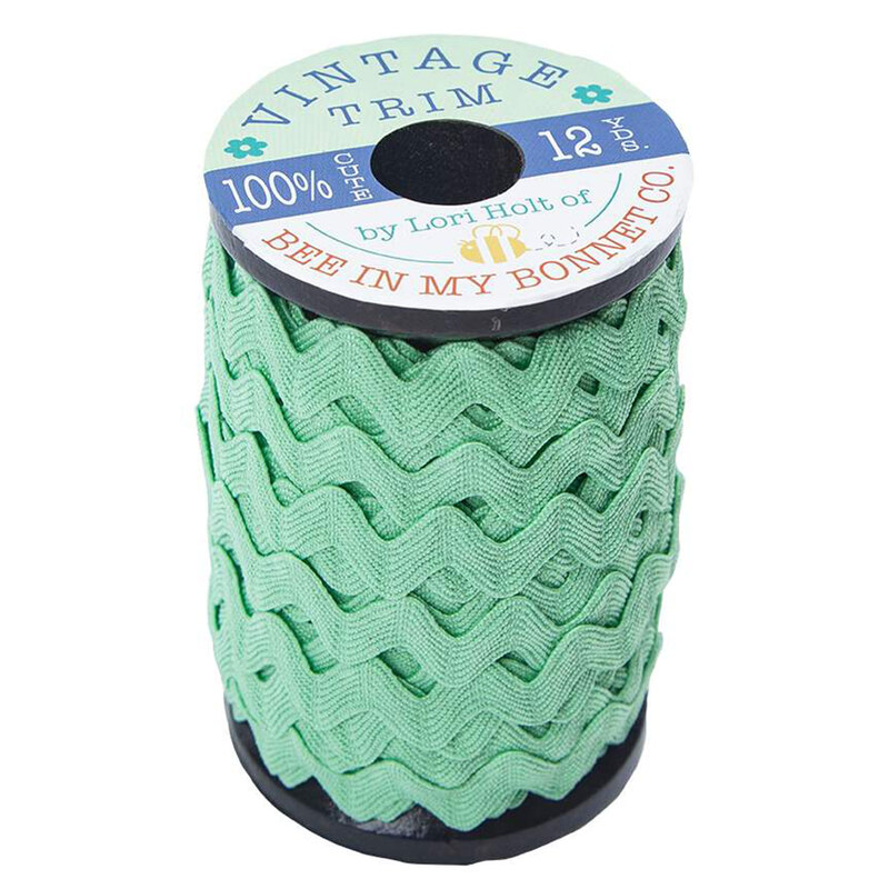 A wooden spool with large mint green ric-rac trim on a white background