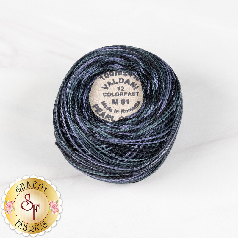 A ball of Valdani Pearl Cotton thread in variegated dark blue, periwinkle, and gray blue, isolated on a marbled white background.