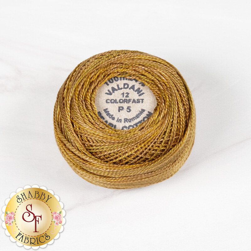 A ball of Valdani Pearl Cotton thread in brassy gold, isolated on a marbled white background.