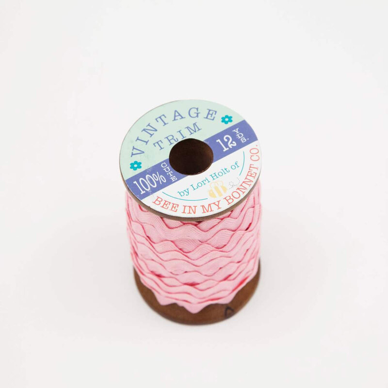 A wooden spool with bubblegum pink ric-rac trim on a white background