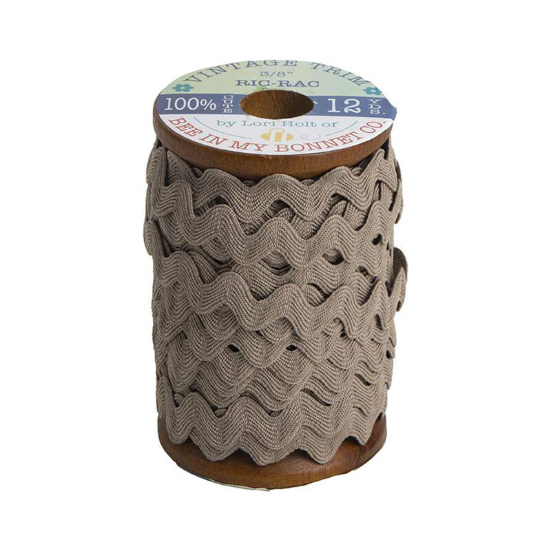 A wooden spool with warm gray ric-rac trim on a white background
