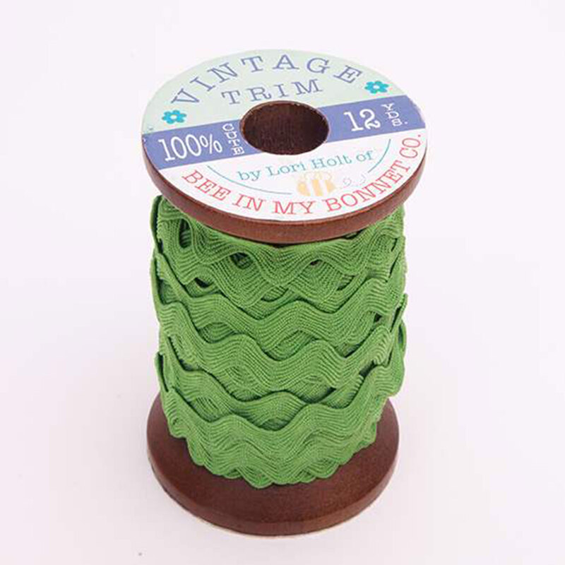 A wooden spool with grass green ric-rac trim on a white background