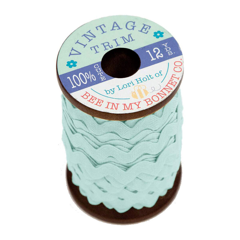 A wooden spool with robin's egg blue ric-rac trim on a white background
