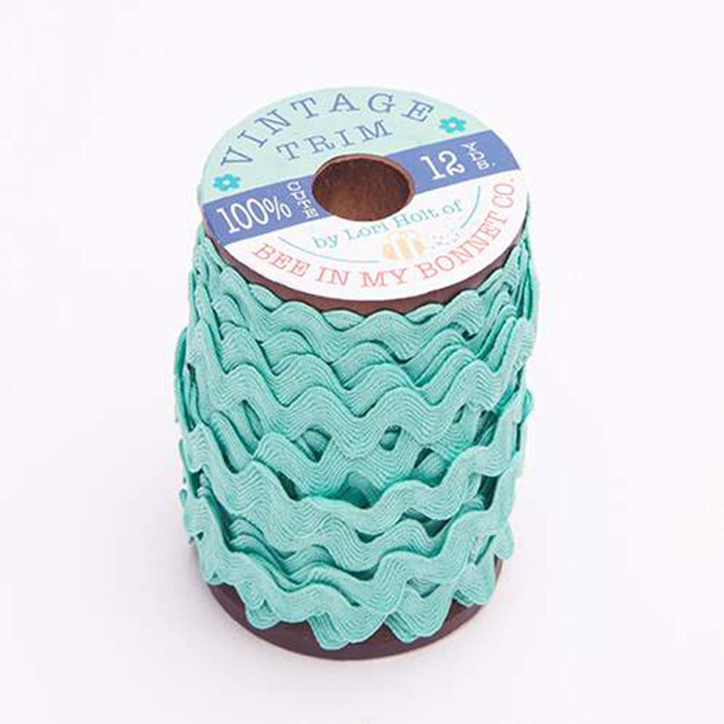 A wooden spool with light turquoise ric-rac trim on a white background