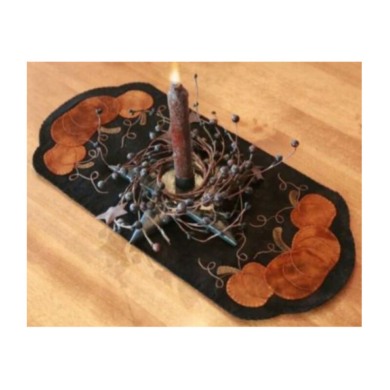 A candle centerpiece on a decorative fabric runner, featuring pumpkins and swirling vine patterns.