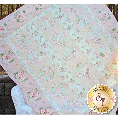 A patterned quilt featuring pastel colors, floral designs, and a patchwork layout, displayed against a natural background.