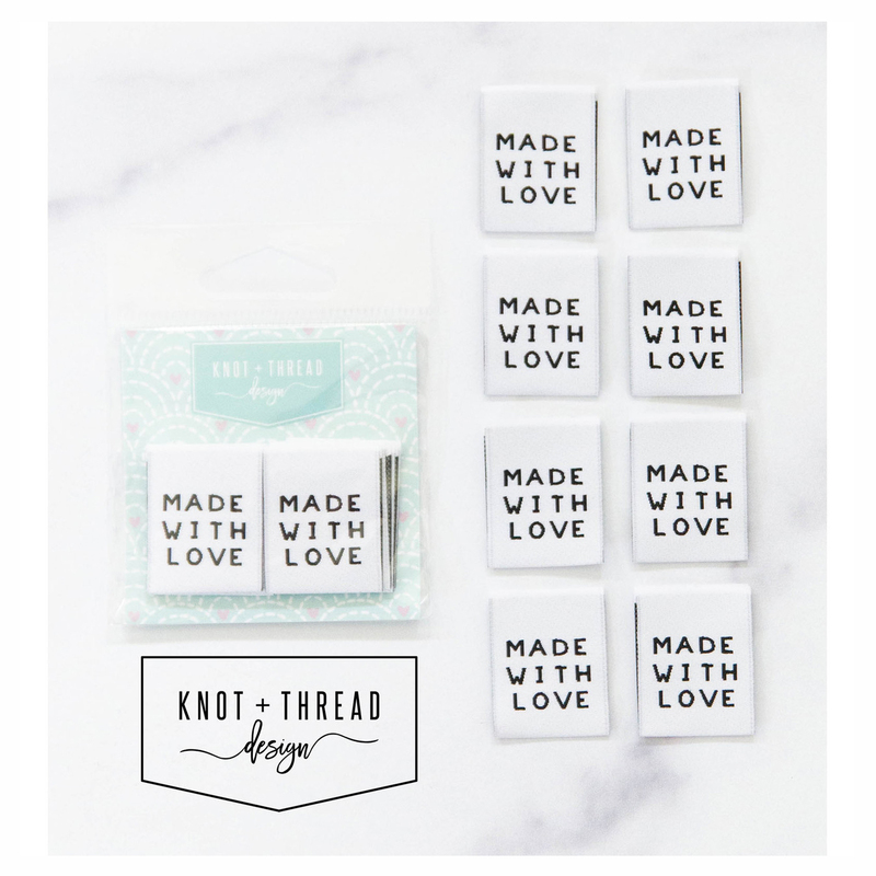 8 "Made with Love" fabric tags lined up and in packaging by Knot and Thread Designs on a white marble background. 