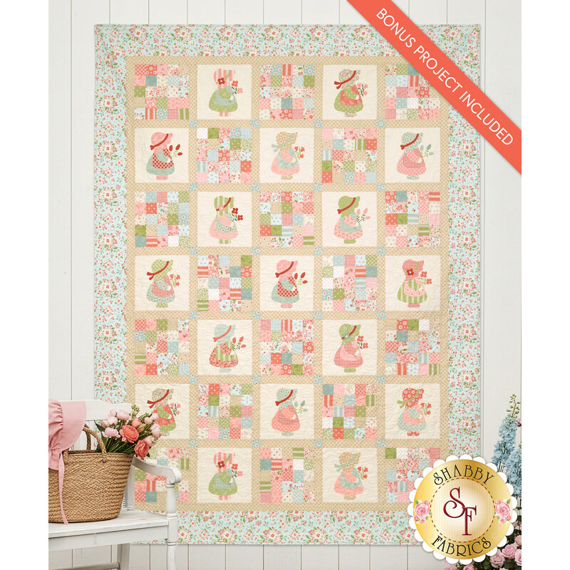 The completed Patchwork Panel Quilt colored in the Sunbonnet collection from Moda Fabrics, hung on a white paneled wall with coordinating florals and décor on either side of the quilt.