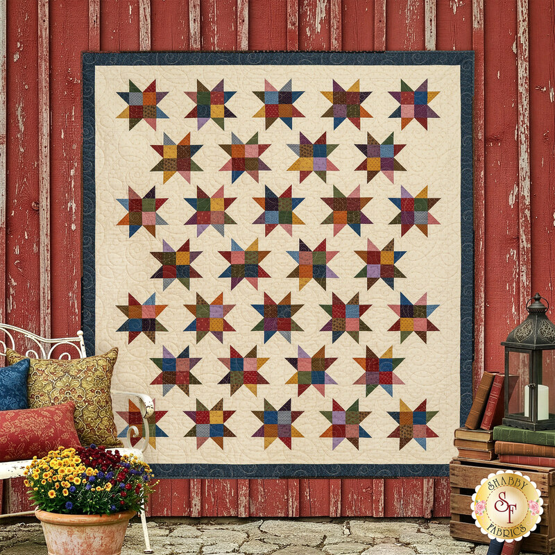 The completed strip friendly quilt kit in muted fabrics from the Prairie Dry Goods II collection by Moda, hung on a rustic red barn surrounded by coordinating décor. 