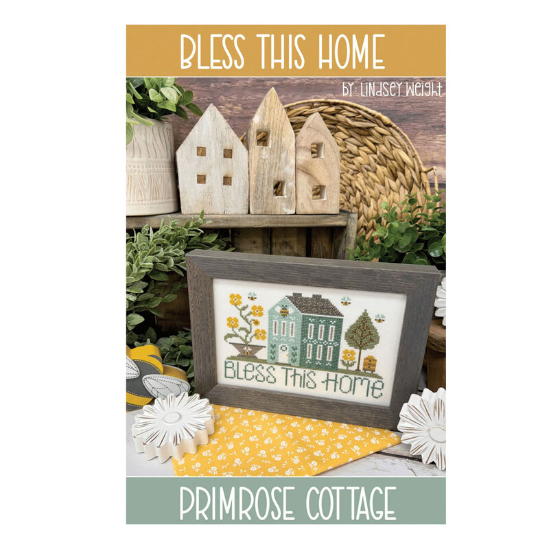 Front of the Bless This Home pattern featuring the framed finished project surrounded by wooden home decor and greenery.