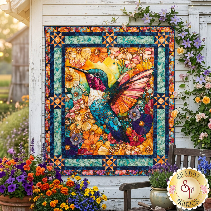 The completed Flight of Beauty Panel Quilt colored in vibrant orange, teal, purple, and magenta fabrics, staged on a rustic white wood wall in a lush, full bloom garden. 