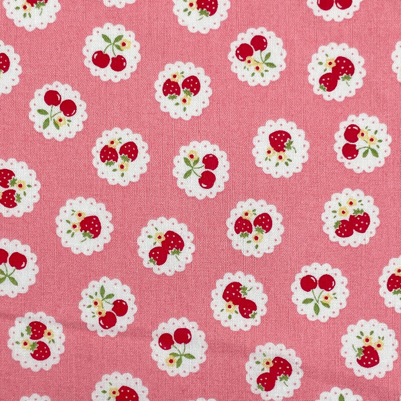 Pink fabric with a pattern of vintage-style medallions filled with assorted fruits like cherries and strawberries.