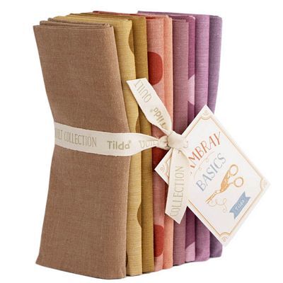 A stacked bundle of assorted Tilda Chambray fabrics in ocher, red-orange, and purple, tied with a label.