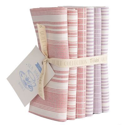 A stacked bundle of assorted Tilda Woven Teal Towel fabrics in white with red and plum accents, tied with a label.