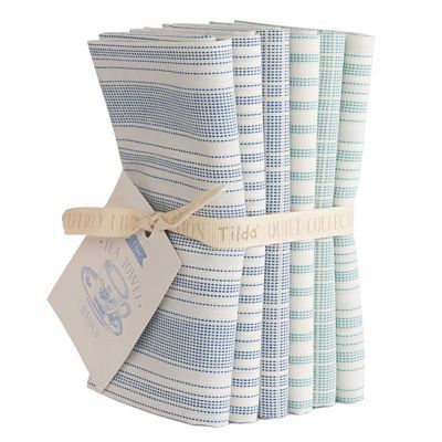 A stacked bundle of assorted Tilda Woven Teal Towel fabrics in white with blue and teal accents, tied with a label.