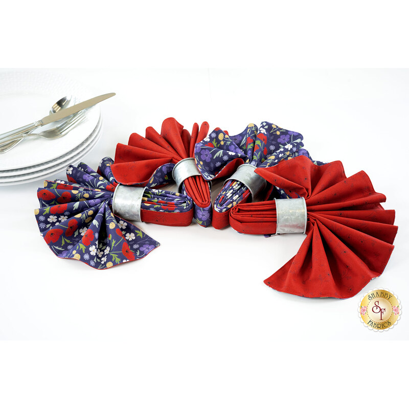 An image of the four napkins colored in the Forever Blooms collection by Lewis & Irene Fabrics, featuring navy blue floral fabric paired with scarlet red fabric and silver rings. A gold Shabby Fabrics logo is in the bottom right corner of the image. 