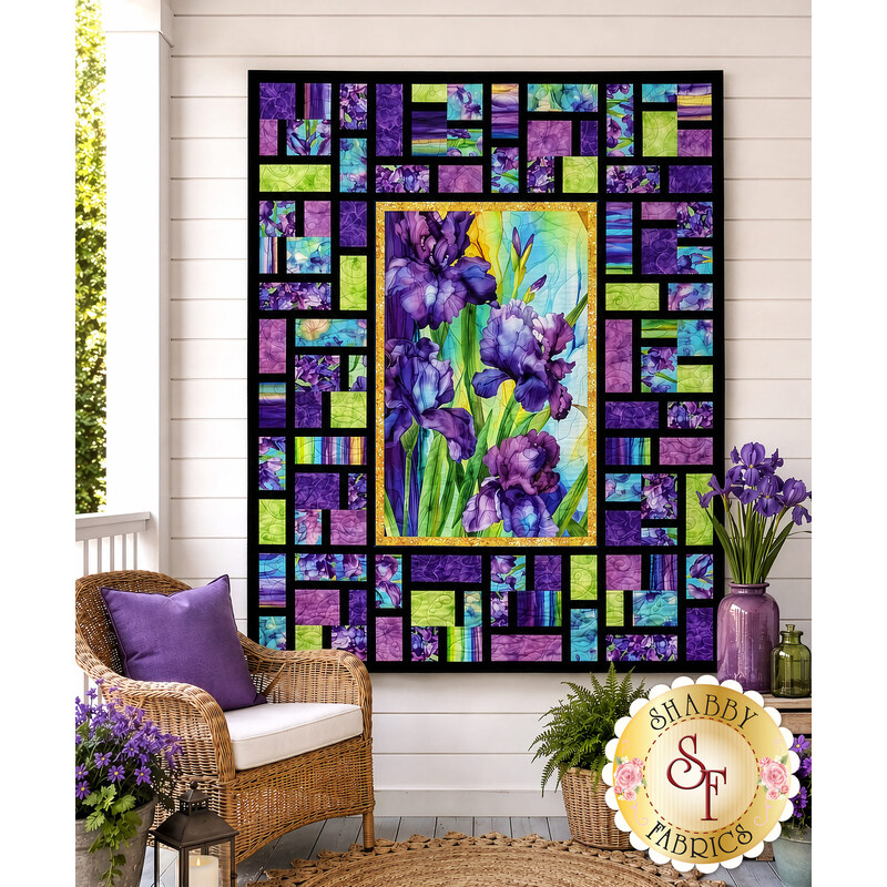 The completed Stained Glass Panel Quilt, colored in bright cerulean, purple, black, and green fabrics from the Infatuation collection by Northcott Fabrics, hung on a white paneled porch wall and staged with coordinating décor.