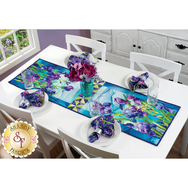 A white dining table staged with a the completed Iris in Bloom table runner, matching napkins, and a vase of coordinating flowers.