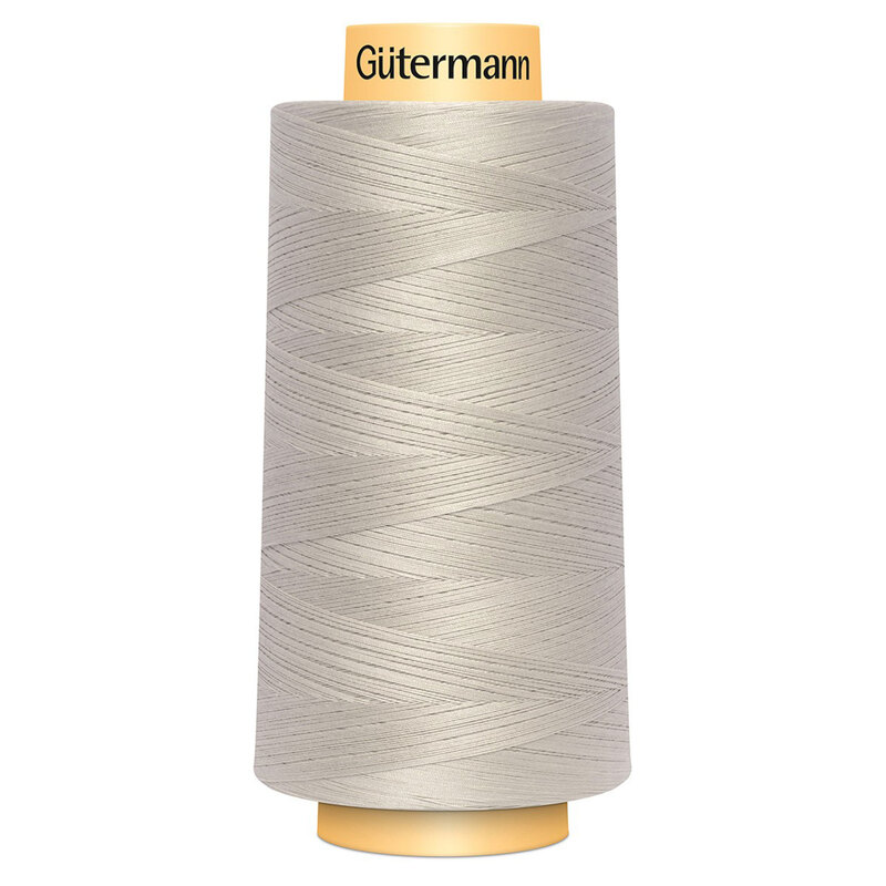 A spool of Gütermann Cotton Thread - Sandy Gray thread on a white background