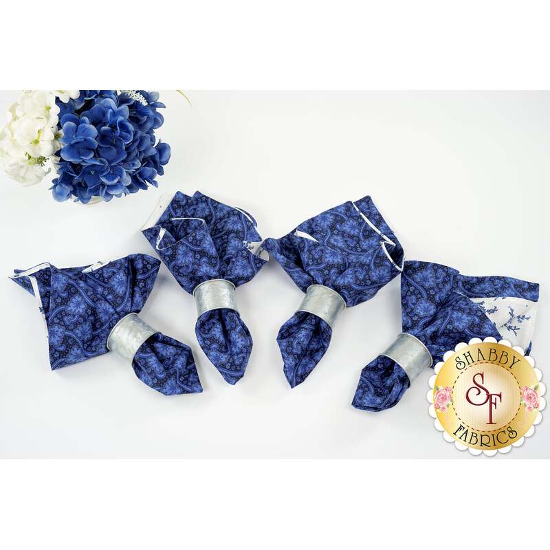 A top-down shot of the four napkins colored in the Blue Belle collection by Maywood Studio, featuring dark blue paisleys paired with simple white florals and silver rings.