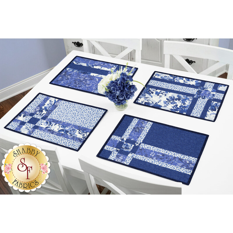 The four completed Fat Quarter Shuffle Mats, colored in dark blue, blue, and white fabrics from the Blue Belle collection by Maywood Studio, set on a white table with coordinating décor. 