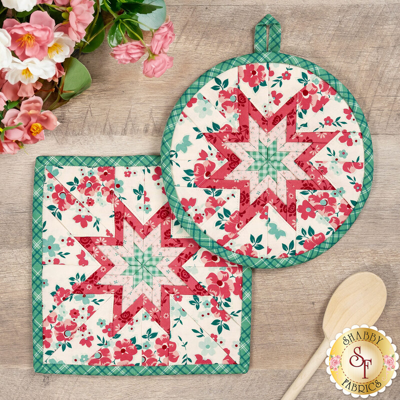 The completed Berry & Sage Folded Star Hot Pad in both the round and square options, staged on a rustic wood table with coordinating décor.