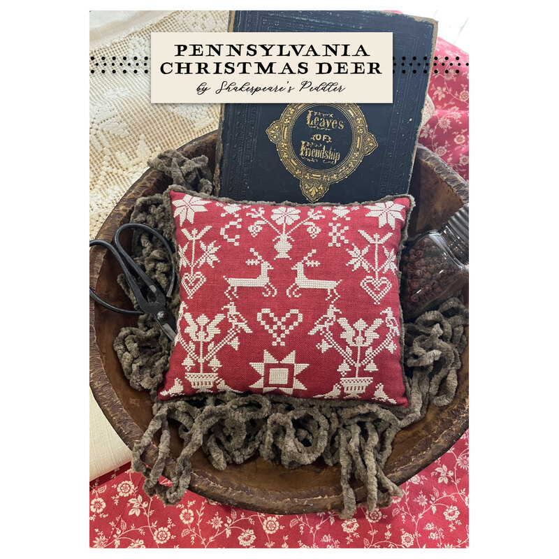 The front of the pattern with a completed cross stitch finished as a pillow in a bowl and surrounded by coordinating décor.