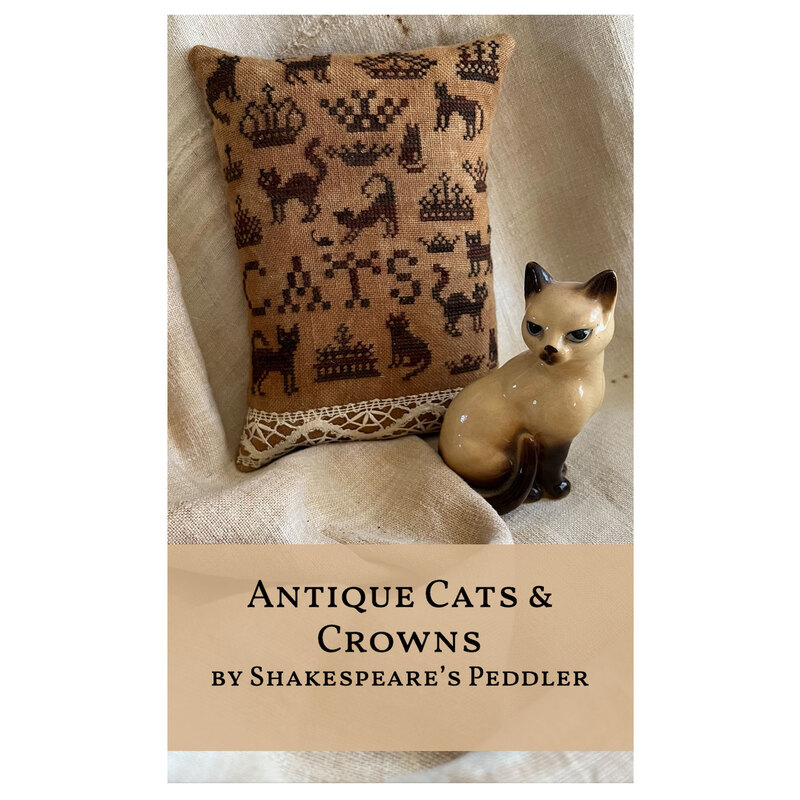 The front of the pattern with the completed cross stitch finished as a pillow, a ceramic cat sits nearby. 