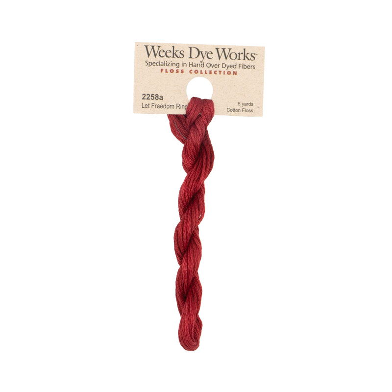 A skein of deep red embroidery floss, twisted and bundled, with a tan label featuring the brand name and color information.