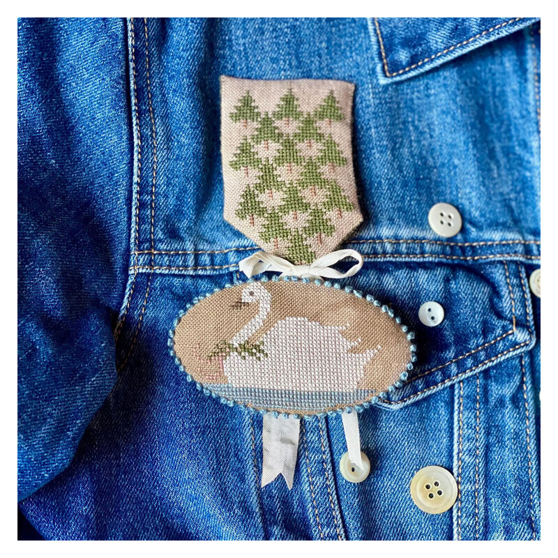 Image of the finished badge project featuring evergreens and a swan swimming.